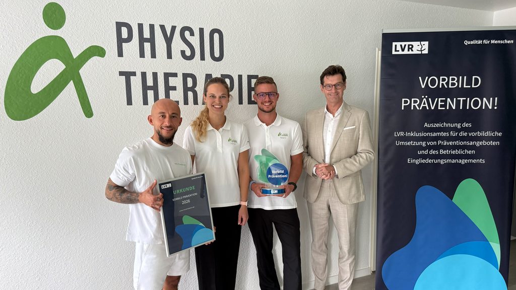 Das Bild zeigt das Geschäftsführenden-Trio von Alpha Physiotherapie und den Leiter des LVR-Inklusionsamtes bei der Prämienvergabe.